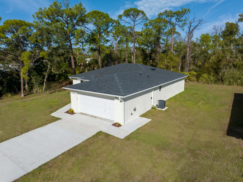 Elevated aerial view of the front side of a single-story home, garage, driveway, and surrounding yard