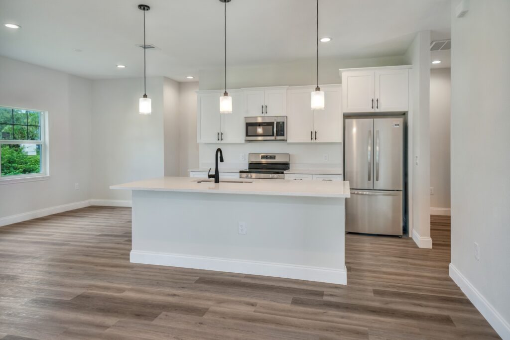 Bright open-concept kitchen with white cabinetry, island seating, pendant lights, and wood-look flooring