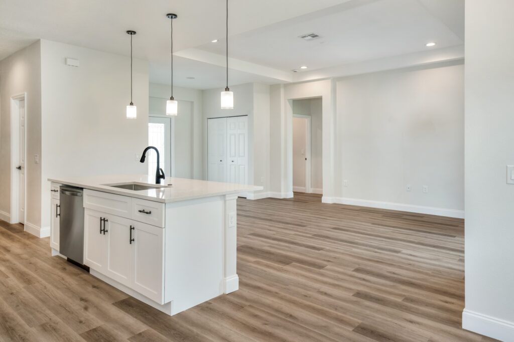 Bright modern kitchen with white cabinetry, island seating, pendant lights, and wood-look flooring