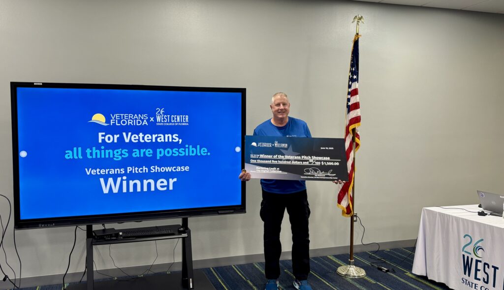 Dan Bidwell holding the winning award beside the 26 West Center Veterans Pitch Competition winner display
